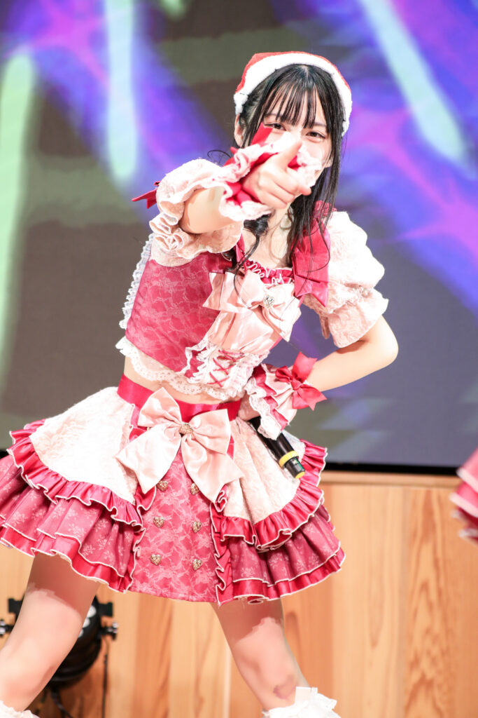 embellir(あんべりー)の水野ひなたちゃんをライブ中に撮影した写真。
この日はクリスマスイベントということでひなたちゃんはサンタの帽子をかぶっている。
こちらを真っ直ぐ見つめて指さしてくれている。
2025年12月14日　としま区民センター多目的ホール　IDOL SODA Stream!!にて撮影。