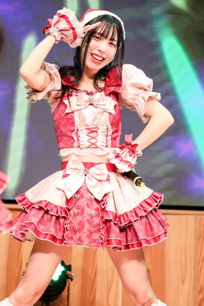 embellir(あんべりー)の水野ひなたちゃんをライブ中に撮影した写真。
この日はクリスマスイベントということでひなたちゃんはサンタの帽子をかぶっている。
こちらを真っ直ぐ見つめながら顔の前で手をひさしのようにして「見つけた」のポーズをしてくれている。
2025年12月14日　としま区民センター多目的ホール　IDOL SODA Stream!!にて撮影。