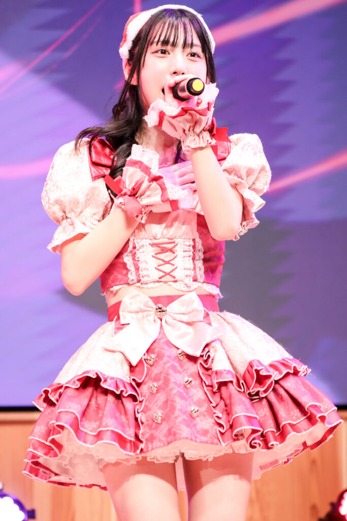 embellir(あんべりー)の水野ひなたちゃんをライブ中に撮影した写真。
サンタ帽子をかぶって髪は巻いている。立ち姿がとても綺麗。
2025年12月14日　としま区民センター多目的ホール　IDOL SODA Stream!!にて撮影。