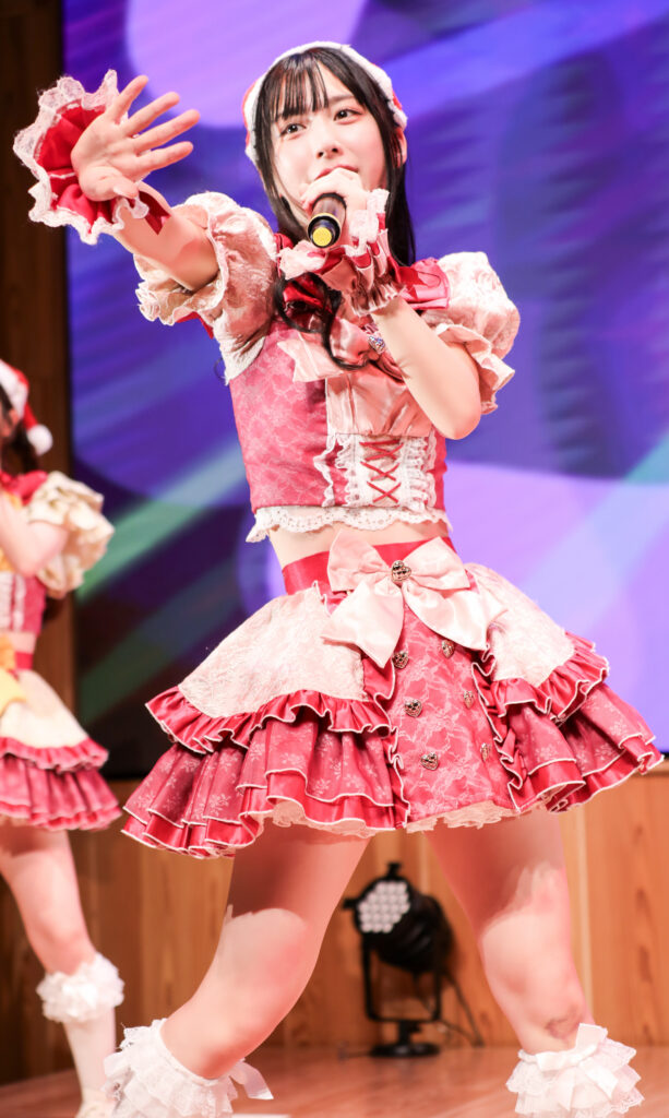 embellir(あんべりー)の水野ひなたちゃんをライブ中に撮影した写真。
サンタ帽子をかぶって髪は巻いている。手をさしのべる仕草がとても尊い。
2025年12月14日　としま区民センター多目的ホール　IDOL SODA Stream!!にて撮影。
