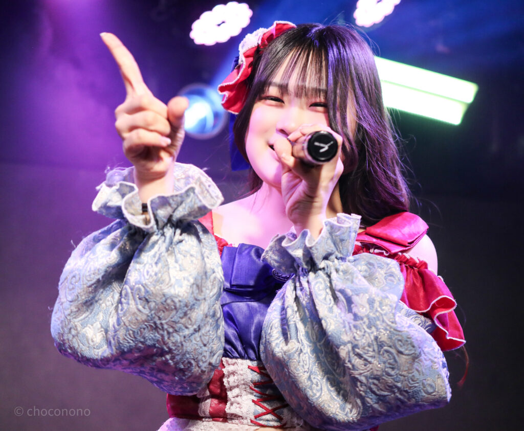 embellir(あんべりー)の恋羽あゆう(こはねあゆう)ちゃんをライブ中に撮影した写真。人差し指をピンと立てながら笑顔で歌唱している。
2025年12月30日GOTANDA G3　FREE BOMBERにて撮影