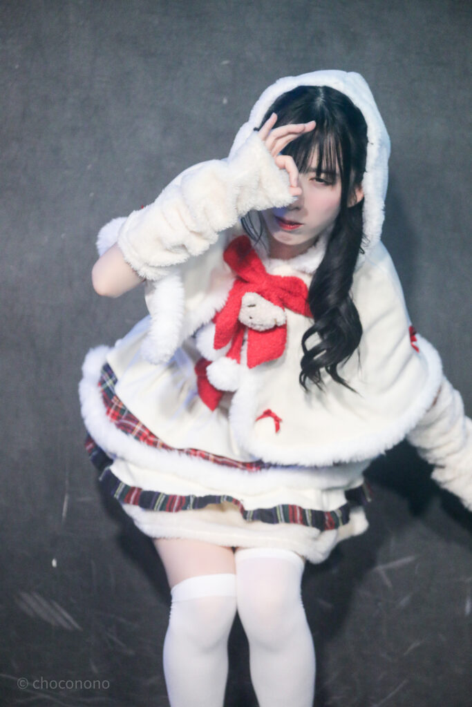 embellir(あんべりー)の水野ひなた(みずのひなた)ちゃんをライブ中に撮影した写真。
ゆきんこ衣装を着ている。
手で輪っかを作ってそこから誰かをのぞき込むようなジェスチャーをしている。
2025年12月25日GOTANDA G3　冠Fes Xmas SP!にて撮影。