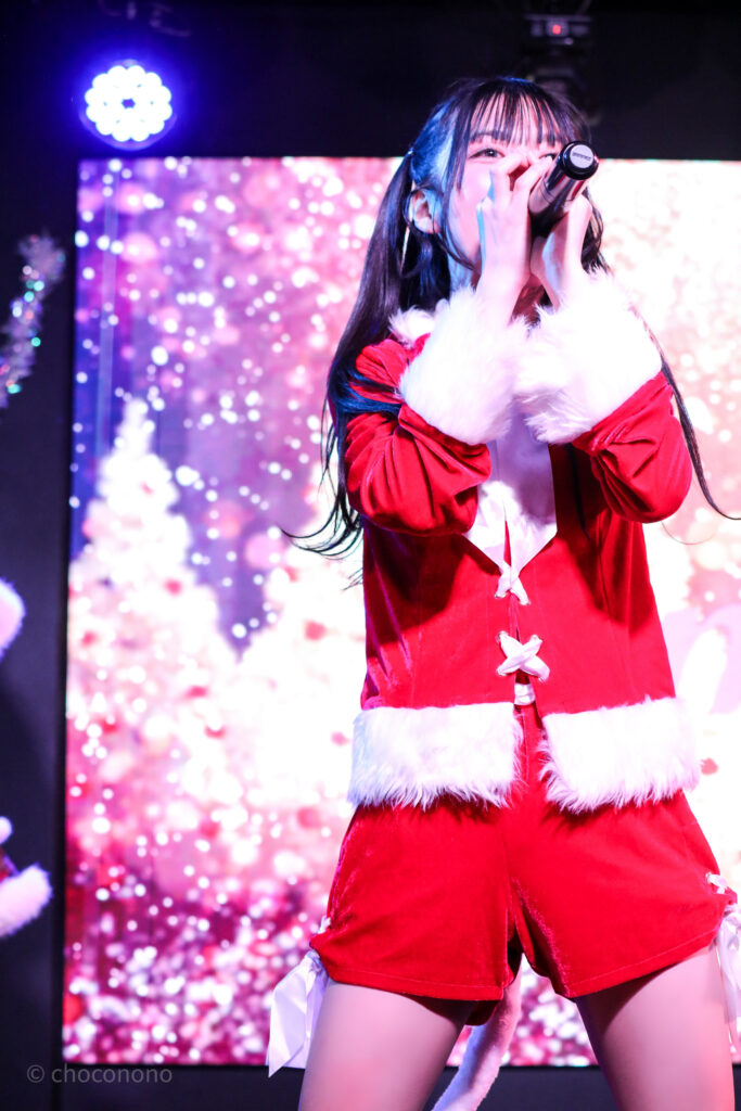 embellir(あんべりー)の水野ひなたちゃんをライブ中に撮影した写真。
パンツスタイルのサンタ服。
真っ直ぐ正面を見据えながら歌唱している。
2025年12月27日　SHIBUYA ONE5　embellir presents Christmas Liveにて撮影。