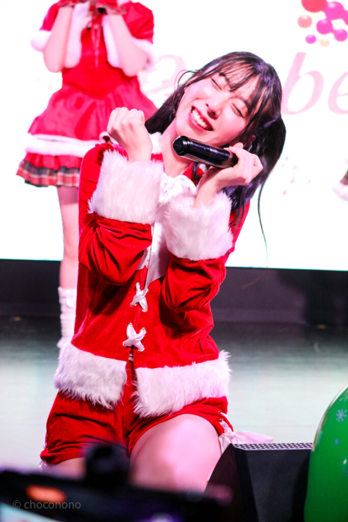 embellir(あんべりー)の水野ひなた(みずのひなた)ちゃんをライブ中に撮影した写真。
パンツスタイルのサンタ服。
にこにこし過ぎて目を閉じてしまっている。可愛い。
2025年12月27日　SHIBUYA ONE5　embellir presents Christmas Liveにて撮影。