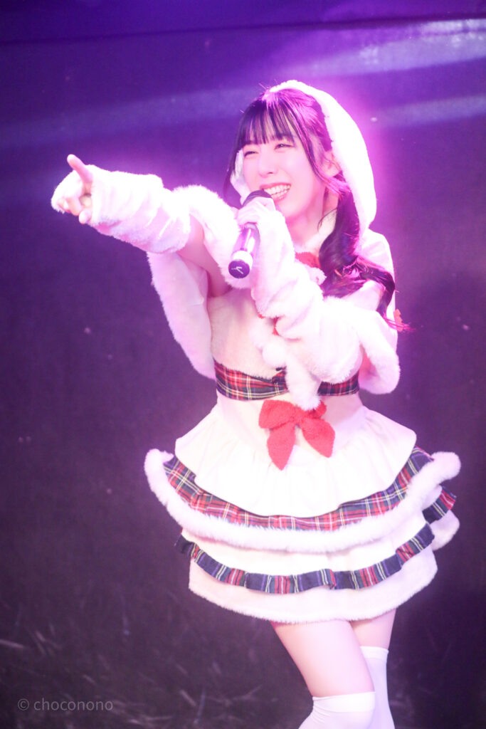 embellir(あんべりー)の水野ひなた(みずのひなた)ちゃんをライブ中に撮影した写真。
ゆきんこ衣装を着ている。
楽しそうに笑顔で歌唱している。フロア後方を真っ直ぐに指さしている。
2025年12月25日GOTANDA G3　冠Fes Xmas SP!にて撮影。