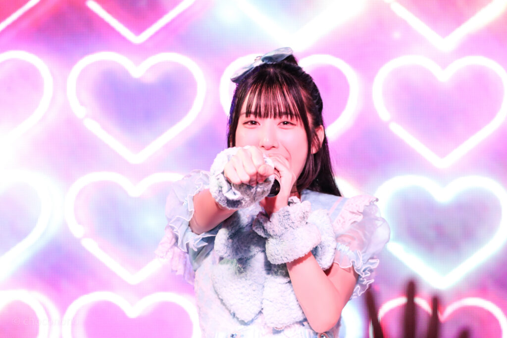 embellir(あんべりー)の水野ひなた(みずのひなた)ちゃんをライブ中に撮影した写真。
拳を前に真っ直ぐ突き出しながら微笑んでいる。
2025年12月31日SHIBUYA ONE5　ONE5 SHUFFLE FESTIVALにて撮影。