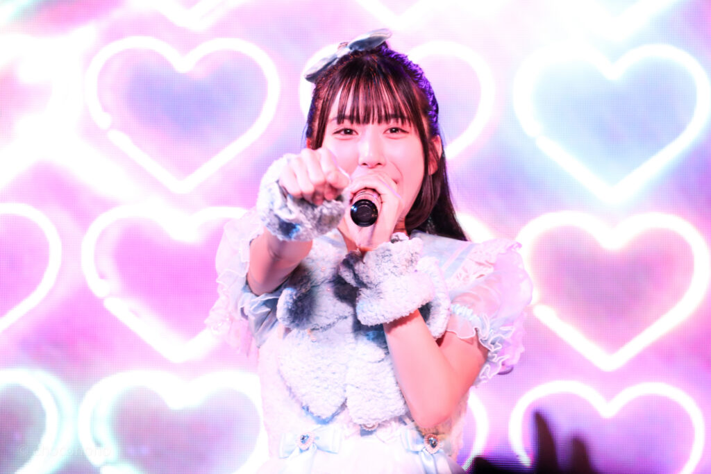 embellir(あんべりー)の水野ひなた(みずのひなた)ちゃんをライブ中に撮影した写真。
拳を前に真っ直ぐ突き出しながら微笑んでいる。
2025年12月31日SHIBUYA ONE5　ONE5 SHUFFLE FESTIVALにて撮影。